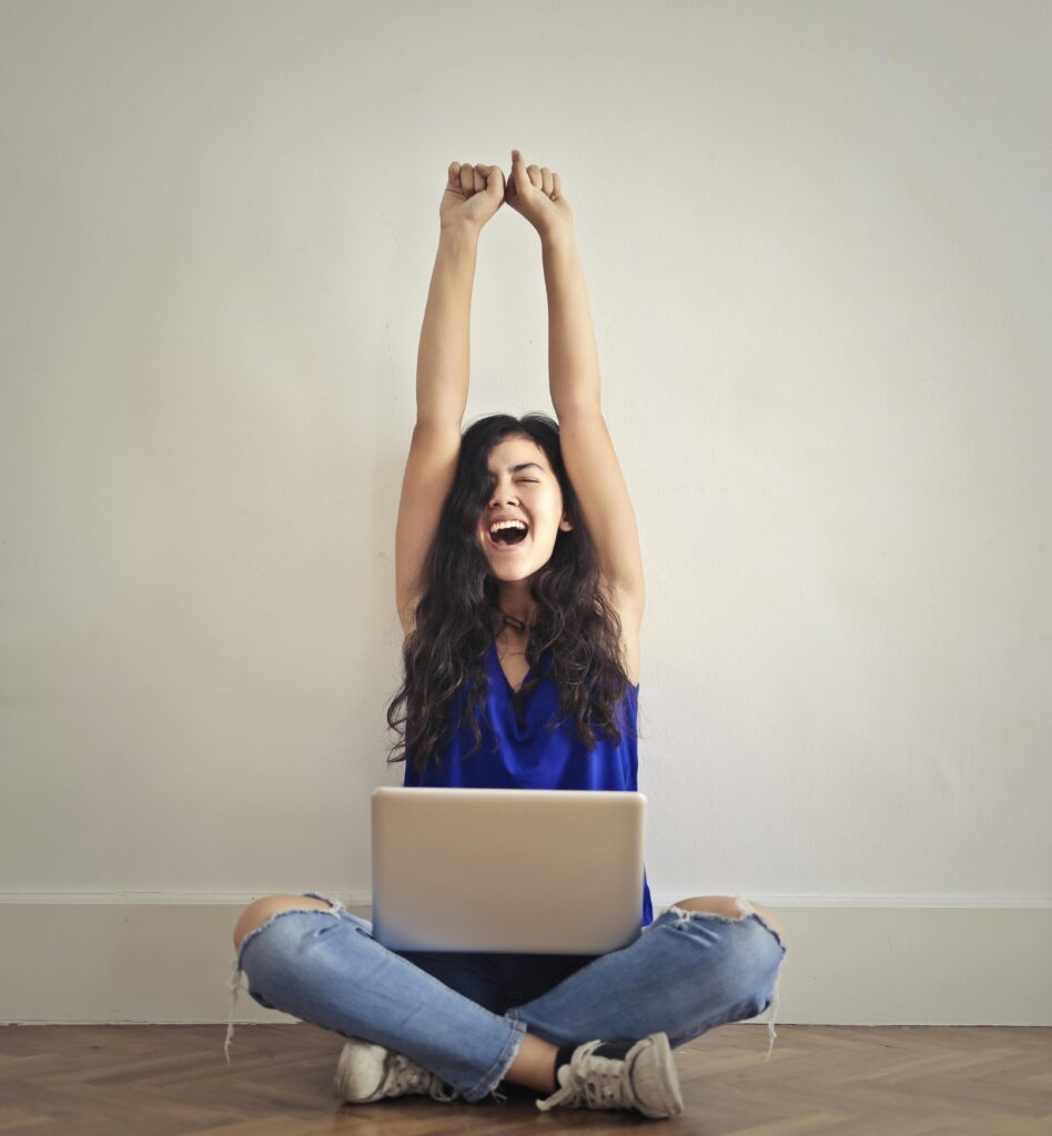 Happy woman with laptop, celebrating success indoors. Arms raised in triumph.