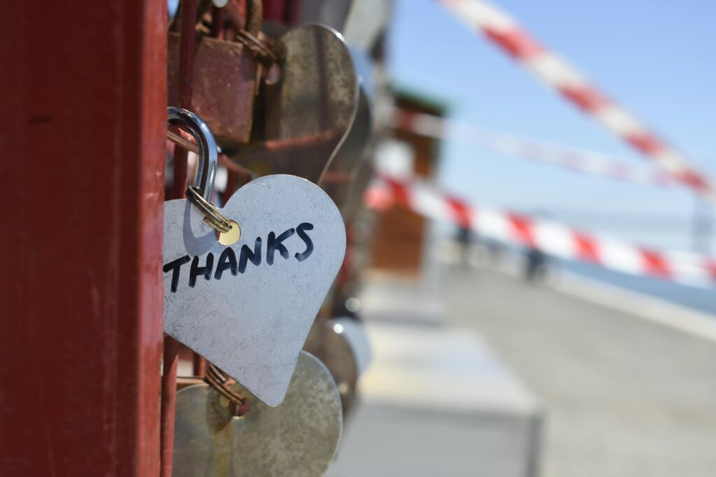 A heart-shaped love lock with 'THANKS' inscribed, hanging on a fence, symbolizing gratitude.